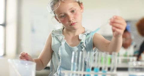 Young girl performing science experiment wearing goggles using pipette, test tubes