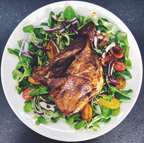 Roasted chicken leg resting on fresh mixed greens salad with cherry tomatoes and red onion