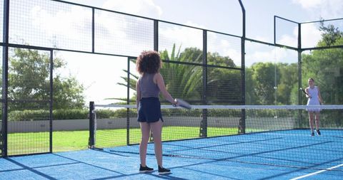 Diverse women playing padel on blue outdoor court holding rackets under sunny sky fitness lifestyle