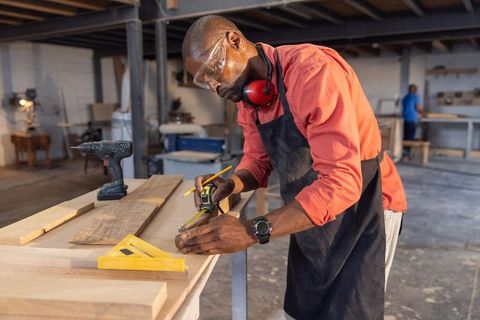 Marking and measuring wooden plank in industrial woodworking shop by skilled craftsman