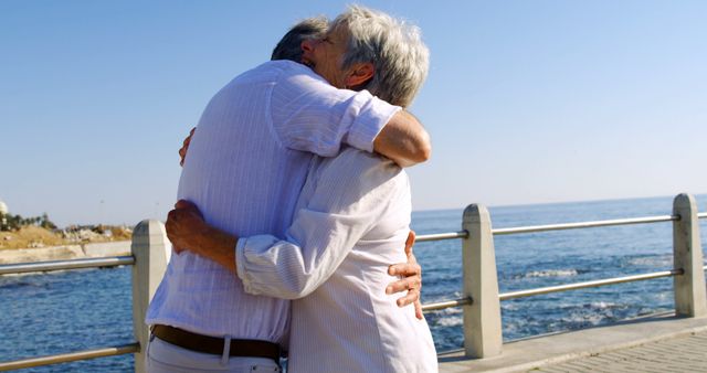 Senior couple embracing near the ocean on a clear, sunny day. Perfect for advertisements or articles about retirement, healthy aging, love and relationships in older age, and outdoor lifestyles for seniors.