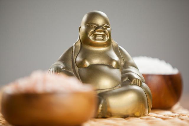 Laughing buddha figurine and sea salt in wooden bowl on mat