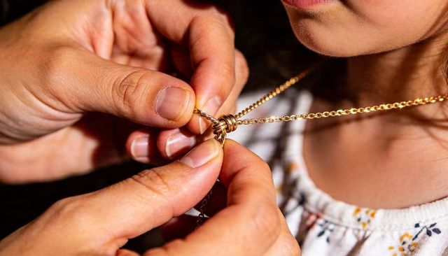 Parent fastening gold necklace on child wearing floral top close-up family moment