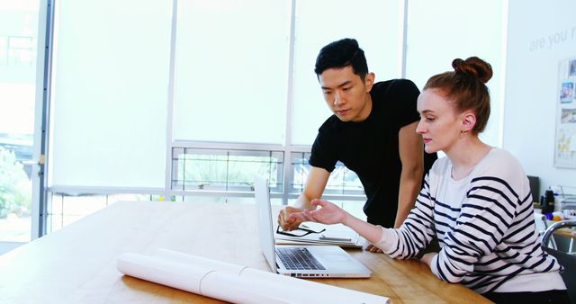 Two designers collaborating at desk with laptop in modern office - Download Free Stock Images Pikwizard.com