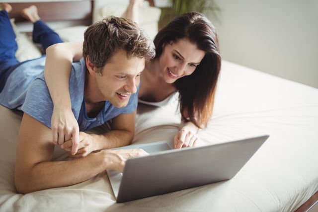 Happy couple using laptop on bed in bedroom at home
