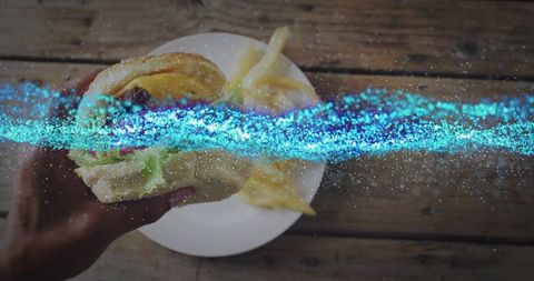 Grasping burger over rustic table with sparkling light accent