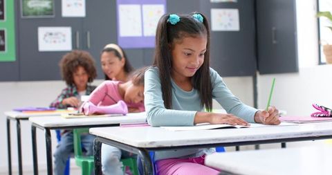 Diligent schoolgirl writing in classroom enhancing learning