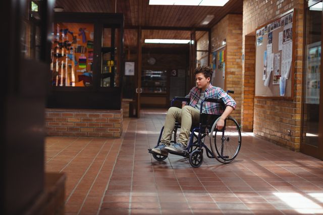 Thoughtful disabled schoolboy on wheelchair in corridor at school