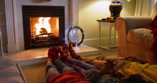 This image captures a family enjoying quality time together in front of a warm and inviting fireplace. The relaxed atmosphere and cozy setting make it perfect for use in holiday-themed promotions, home comfort advertisements, and family-centered campaigns.