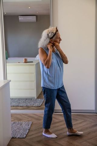 Senior woman dressing in bedroom with modern interior reflection
