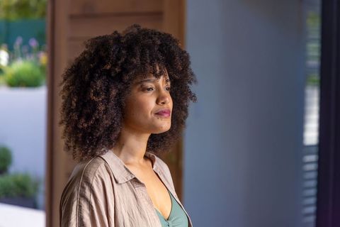 African american woman standing gazing through doorway wearing beige shirt and green camisole