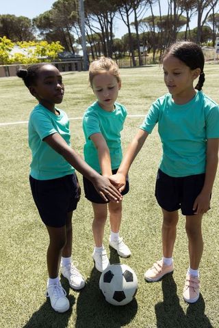 Youth soccer team huddle stacking hands over ball on sunny artificial turf