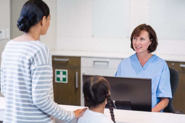Nurse in blue scrubs assisting a patient and her child at the hospital reception desk. Ideal for use in healthcare, medical services, patient care, hospital administration, and family health-related content.
