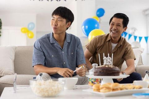 Asian friends celebrating birthday with chocolate cake and balloons in cozy living room