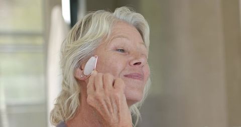 Senior woman using rose quartz facial roller practicing gentle home skincare routine