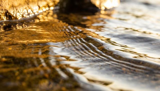Shimmering golden ripples washing over shallow pebble shoreline at sunset closeup