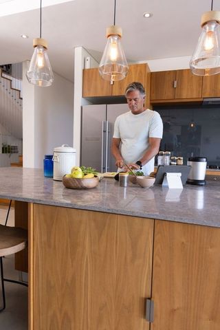 Mature man chopping vegetables at modern kitchen island with tablet and pendant lights