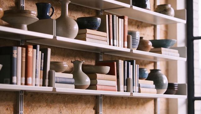 Minimalist wall shelving with stacked books and ceramic vases by windowlight neutral interior