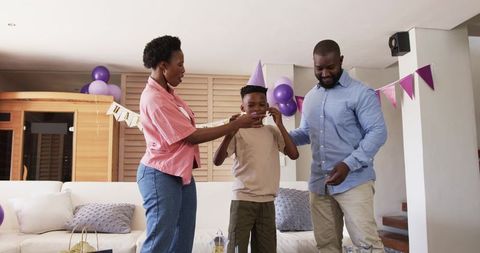 African American Parents Feeding Son Birthday Cake in Living Room Party Celebrating Together