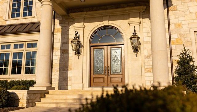 Grand double wooden doors framed by stone columns and glowing in warm evening light