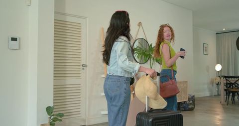 Friends arriving at modern rental carrying suitcase and straw hat, casual summer travel