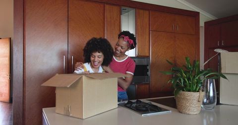 Diverse Female Couple Unpacking Boxes Together in New Kitchen