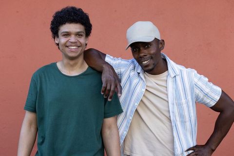 Smiling african american man and friend leaning casually against warm terracotta wall
