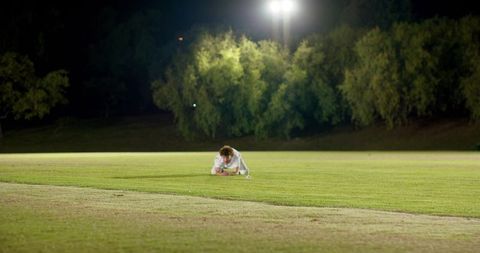 Solitary man crouching on illuminated sports field at night under floodlights