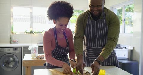 Couple cooking together in bright home kitchen wearing matching striped aprons