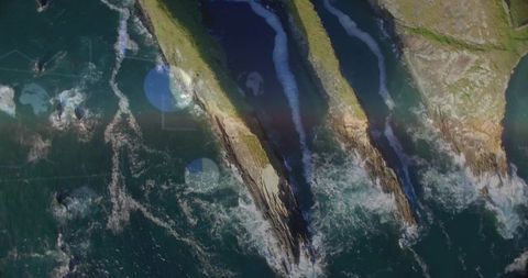 Aerial view showing three sea stacks with grassy tops and choppy waves on rugged coastline