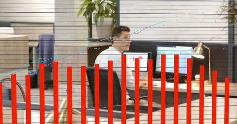 Male professional working at dual monitors with financial analytics overlay and red chart