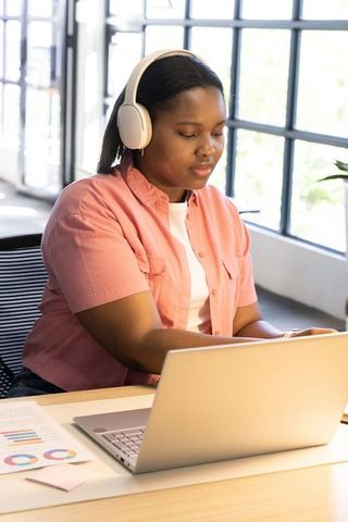 African american woman wearing headphones working on laptop in bright minimalist workspace