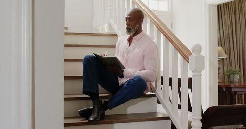 Senior Man Sitting on Stairs Writing in Notebook at Home