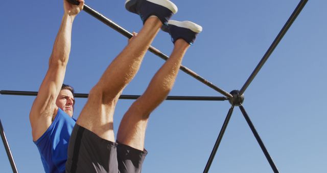 Man in athletic clothing performing a strength-training exercise on an outdoor pull-up bar during a sunny day. Perfect for promoting fitness activities, workout routines, health and wellness programs, exercise equipment, and active lifestyle campaigns.