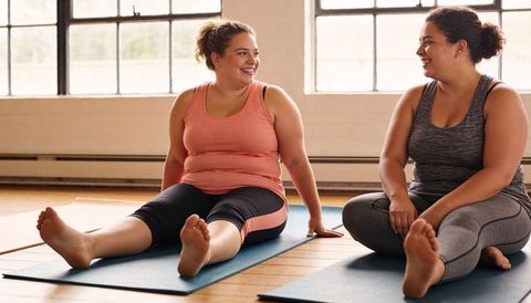Plus-size women smiling, chatting on yoga mats in bright studio embracing body positivity