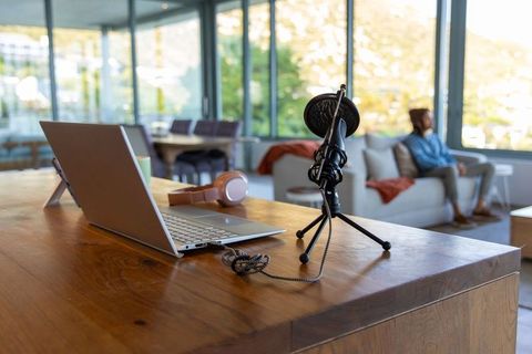 Recording podcast from modern home office with laptop, mic, headphones and relaxed host