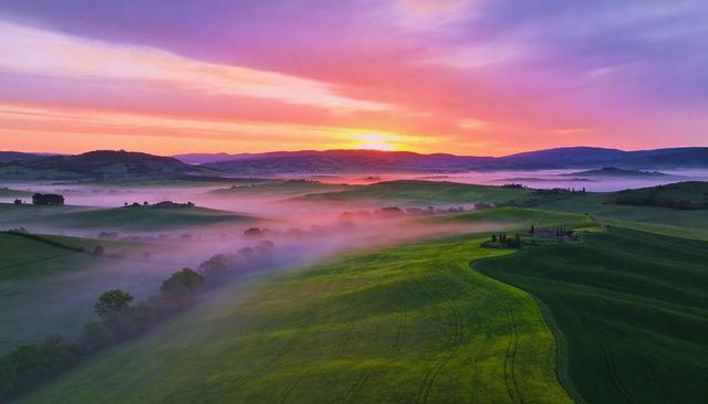 Sunrise fog rolling over green farmland hills creating vibrant misty pastoral panorama