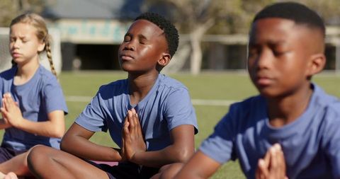 Multiracial teens practicing outdoor meditation on school field for mindfulness