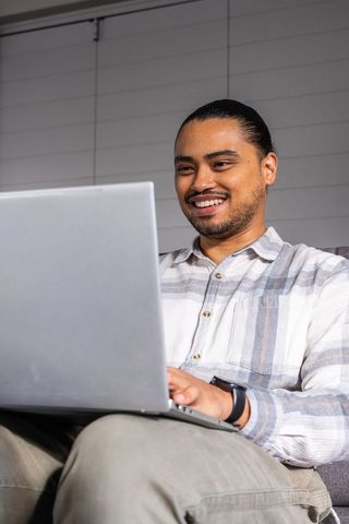 Smiling asian man working on laptop at home sofa, remote work digital lifestyle