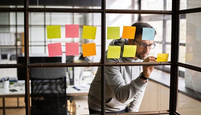 Focused professional writing colorful sticky notes on glass partition for agile planning