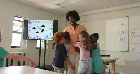 Black teacher hugging and encouraging diverse elementary students smiling in classroom