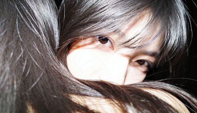 Mysterious asian woman peeking through long dark hair closeup portrait with bangs