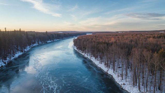 Aerial view of partly frozen river winding through snow-covered boreal forest at sunrise