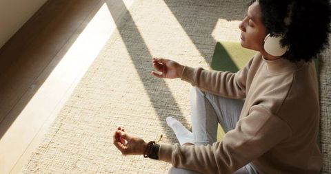 African american man meditating with headphones in sunlit room for mindfulness relaxation