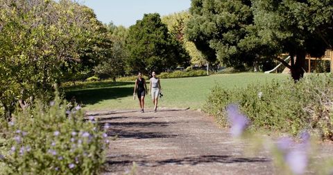 Diverse friends strolling in sunlit park holding athletic shoes