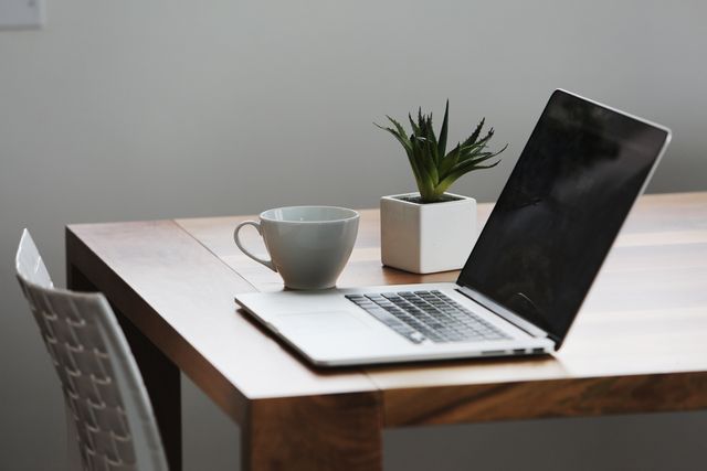 This image shows a minimalist workspace featuring a laptop, coffee mug, and a potted plant on a wooden table. Ideal for articles or advertisements about remote work, home office setups, productivity tips, or modern work environments.