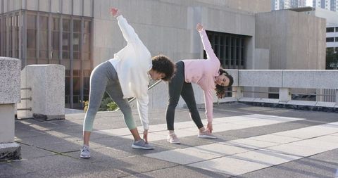 Multicultural women stretching on urban rooftop overlooking city skyline morning workout