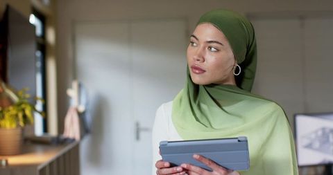 Indian businesswoman in green hijab using tablet in modern minimalist office