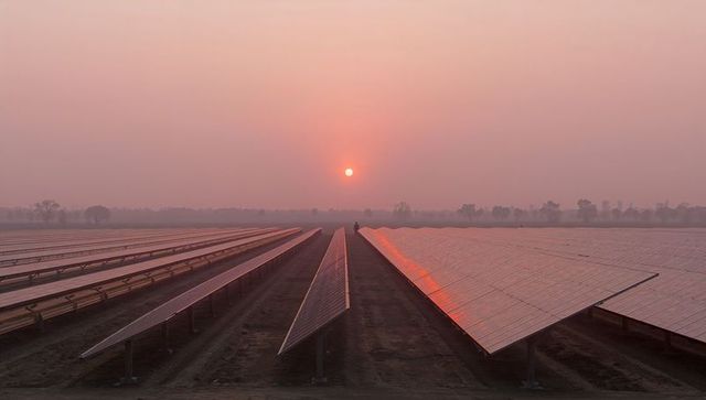 Sunrise reflection across vast solar panel array on rural farm with silhouetted worker