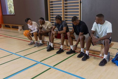 Multicultural basketball teammates sitting on bench exchanging tips and building camaraderie